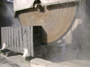 Overhead crane lifting raw granite block at processing facility